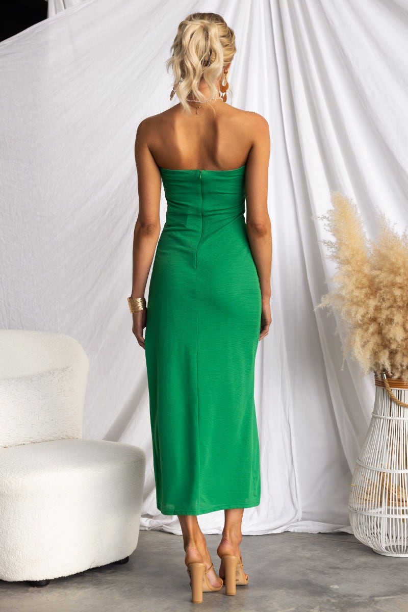 Back view of a woman wearing a green strapless midi dress with ruching and split at the front, showcasing its elegant design.