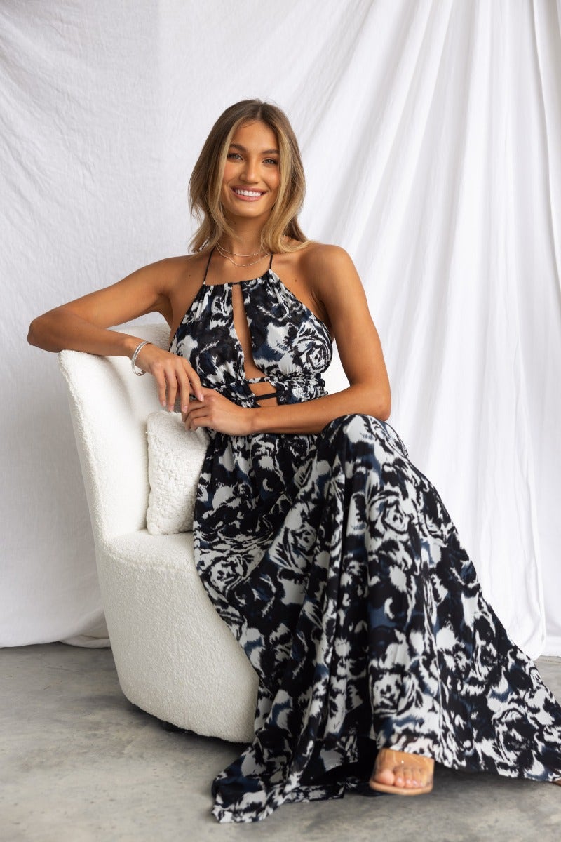 Model wearing Kariah Maxi Dress featuring adjustable halter neckline and floral print, sitting elegantly.