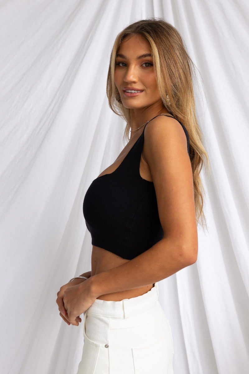 Carrie Top in black ribbed knit with a square neckline, worn by a model with long hair, paired with white pants.