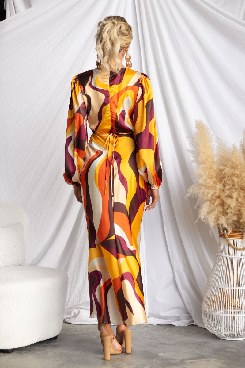 Back view of a model wearing a vibrant multicolored satin maxi dress with cut-out waist and tie detail.