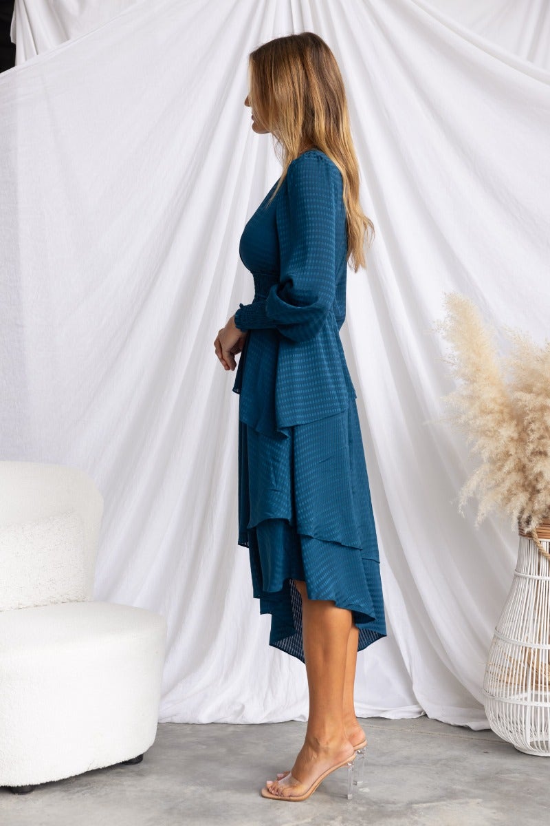 Model wearing a teal Briena Midi Dress with a V-neckline and multi-tier ruffle skirt, side view.