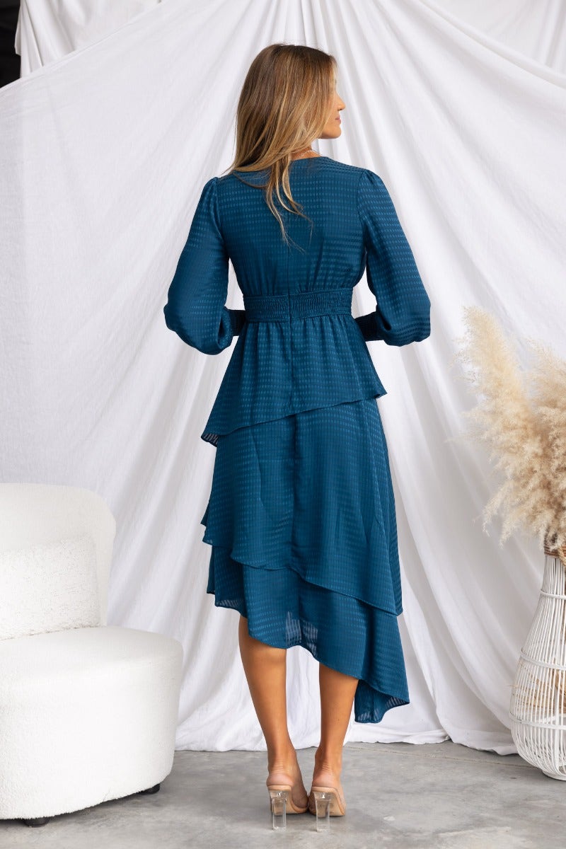 Back view of Briena Midi Dress showcasing its asymmetrical hemline and tiered ruffle design in teal.