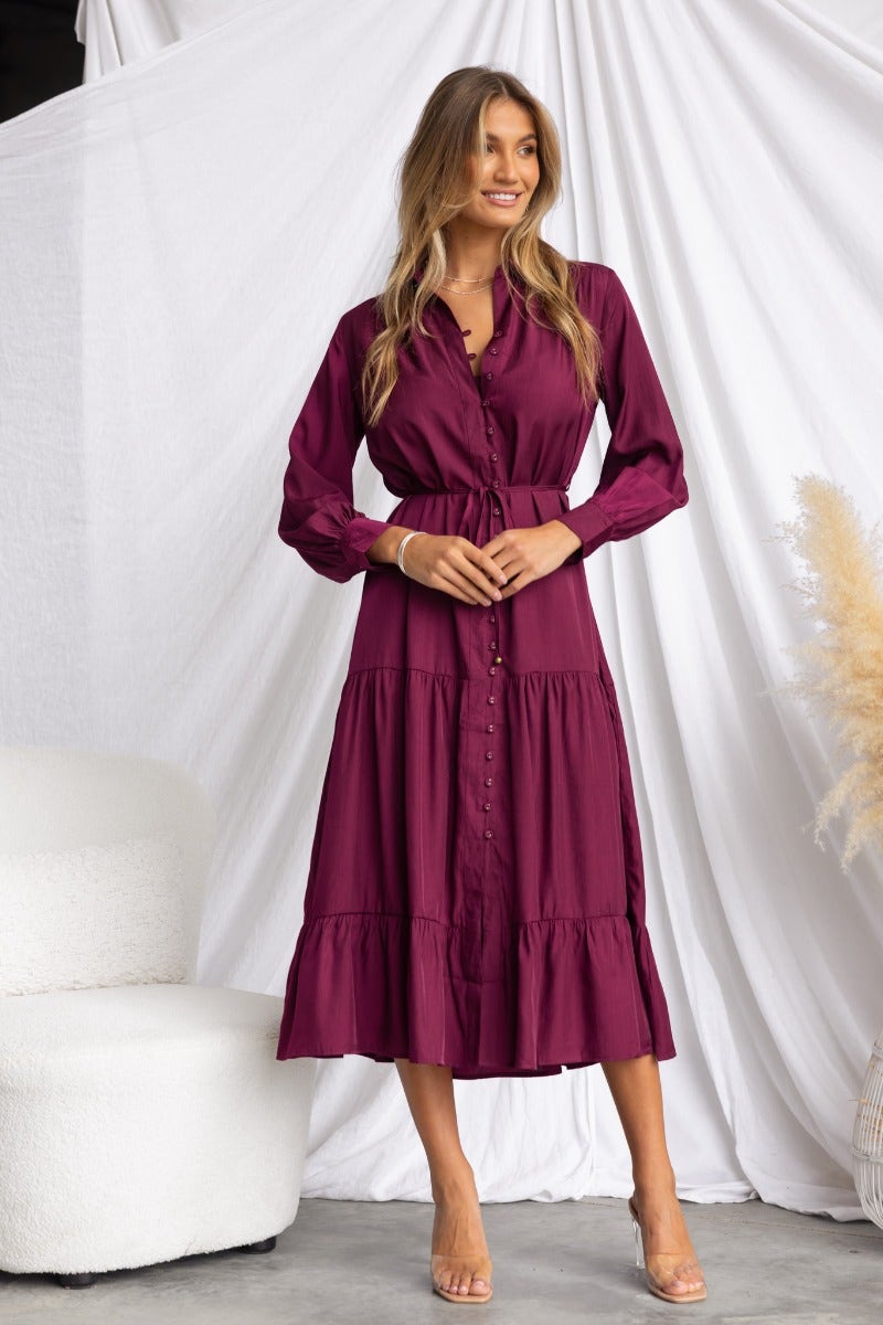 Model wearing an exquisite midi dress in burgundy with collar and button-up front, styled with sandals.