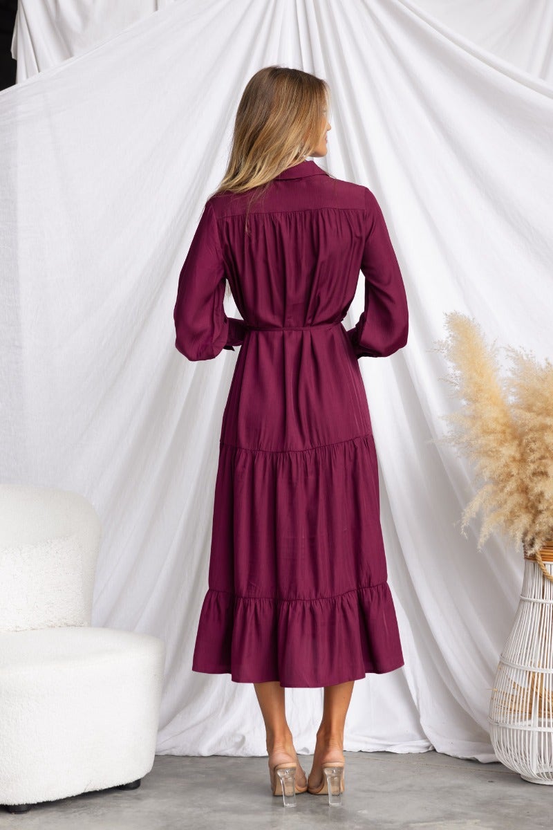 Back view of a woman wearing a burgundy midi dress with a tiered skirt and puff sleeves, showcased in a stylish interior.