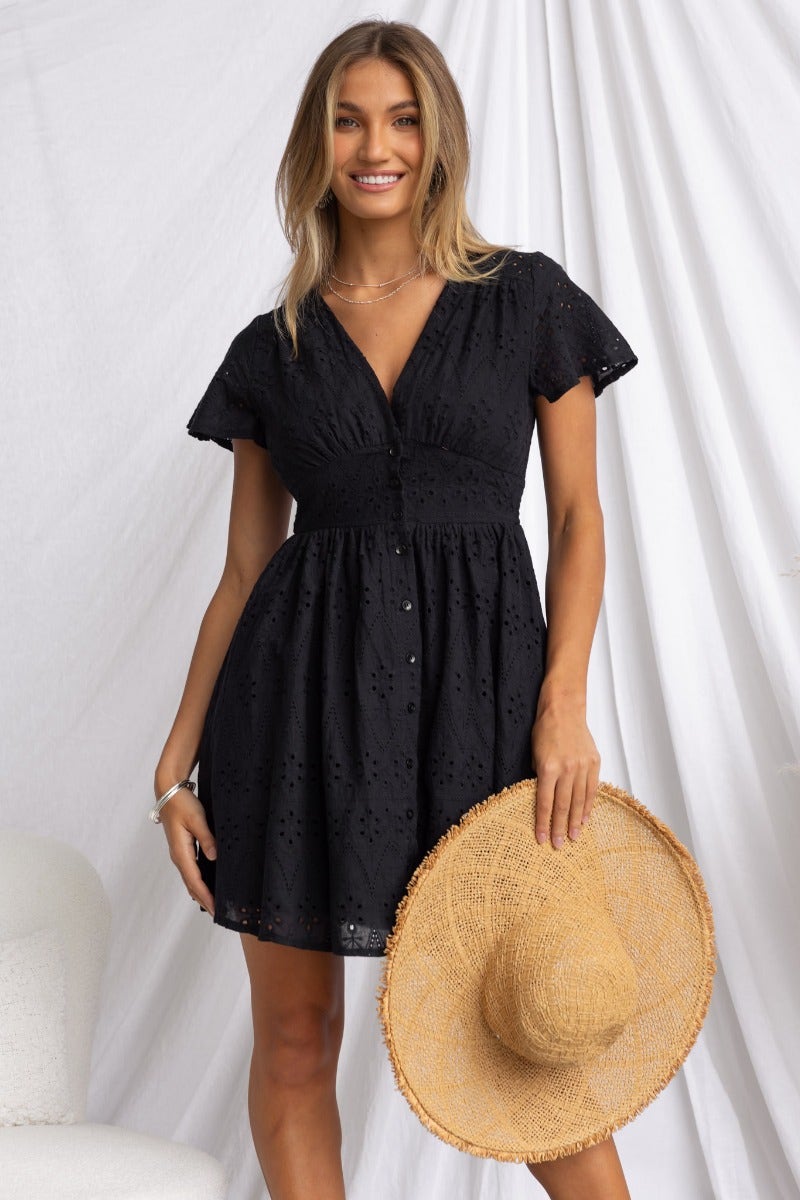 Melita models a black Anglaise dress with V-neckline and button-up front, styled with a straw hat.