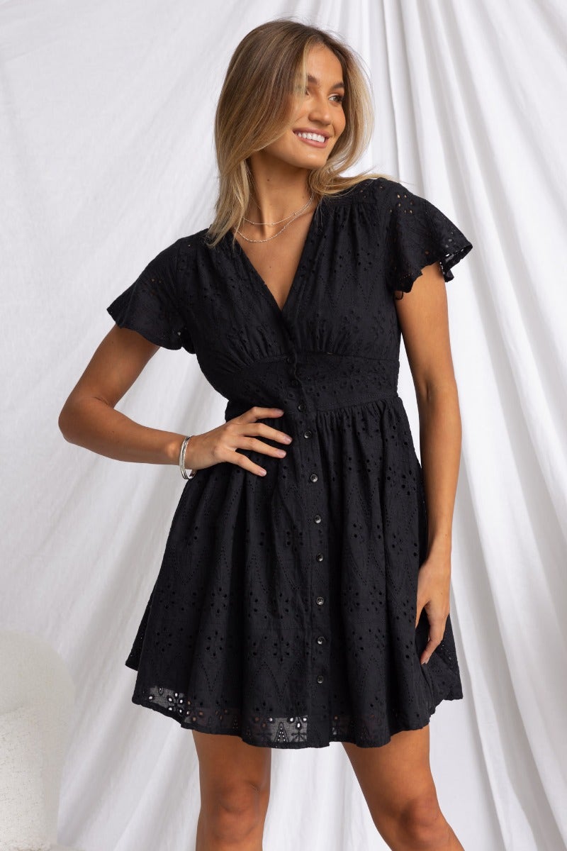 Black Anglaise Udela Dress with V-neckline and button-up front, styled by a model with a joyful expression.