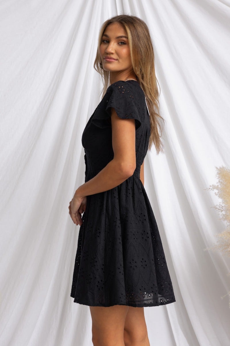 Model wearing a black Anglaise material dress with a V-neckline and button-up front, styled gracefully.