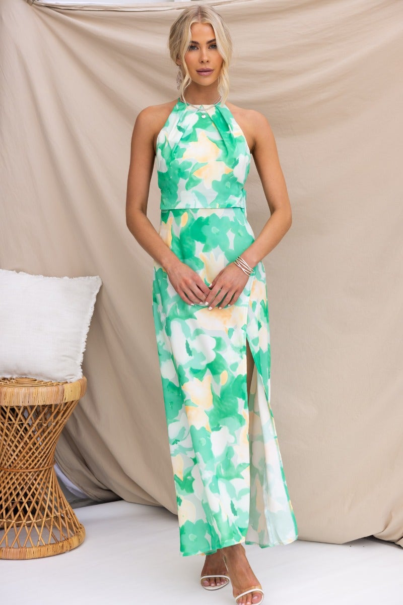 Model wearing a Tangelo Maxi Dress with a floral green print, adjustable tie straps, and an asymmetrical hemline.