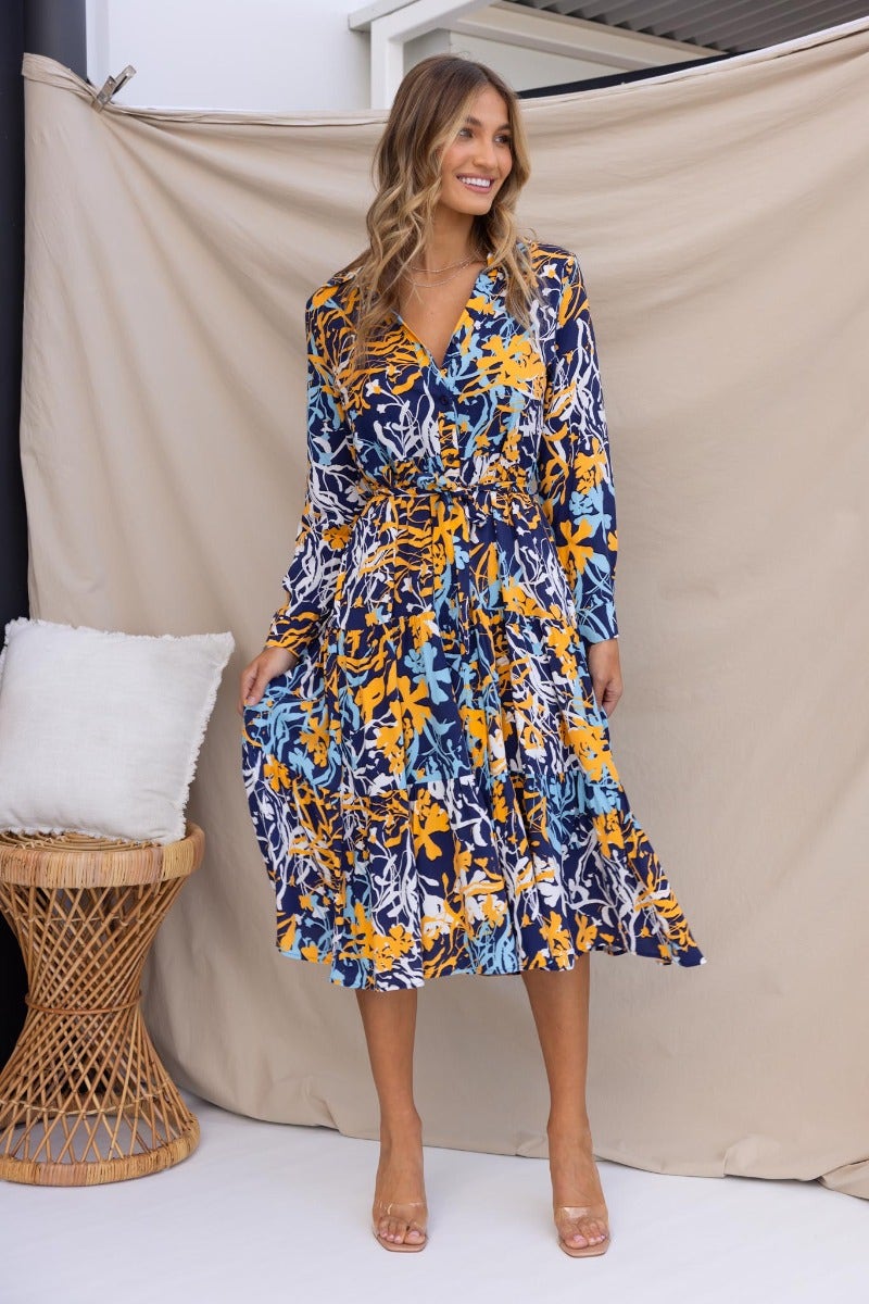 Model wearing Chandra Midi Dress, a navy floral print, featuring a collar, button-up front, and removable tie.