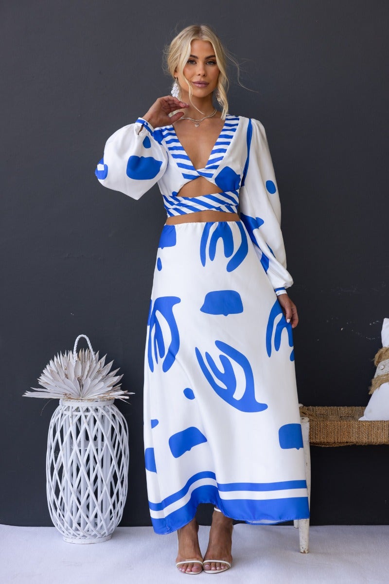 Model wearing Qasim Maxi Dress with bold blue patterns, featuring a twist detail and cut-out at the waist, styled for summer.