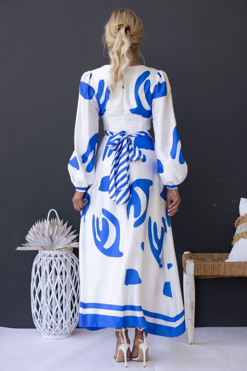 Back view of Qasim Maxi Dress, featuring blue abstract patterns and a tie detail, styled with elegant heels.