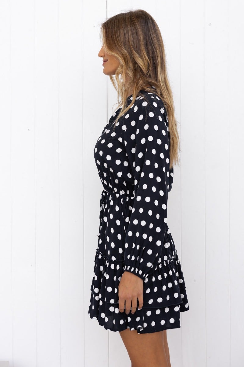Side view of a navy polka dot dress with a V-neckline, button-up bust, and elastic cuffs, showcasing a relaxed fit.