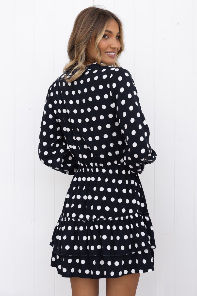 Back view of a navy polka dot dress with elastic cuffs and ruffled hem, perfect for casual outings.
