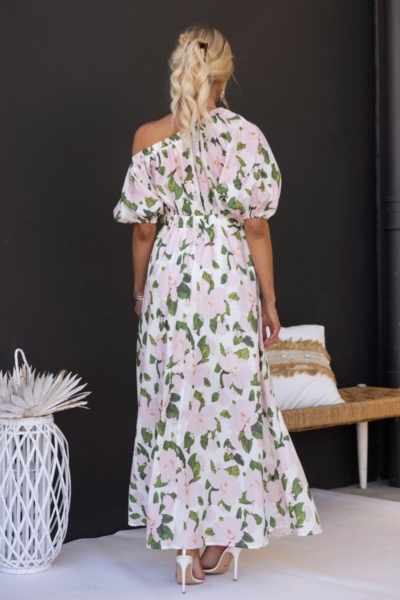 Back view of a woman in a floral print off-shoulder maxi dress, showcasing its puff sleeves and elegant design.