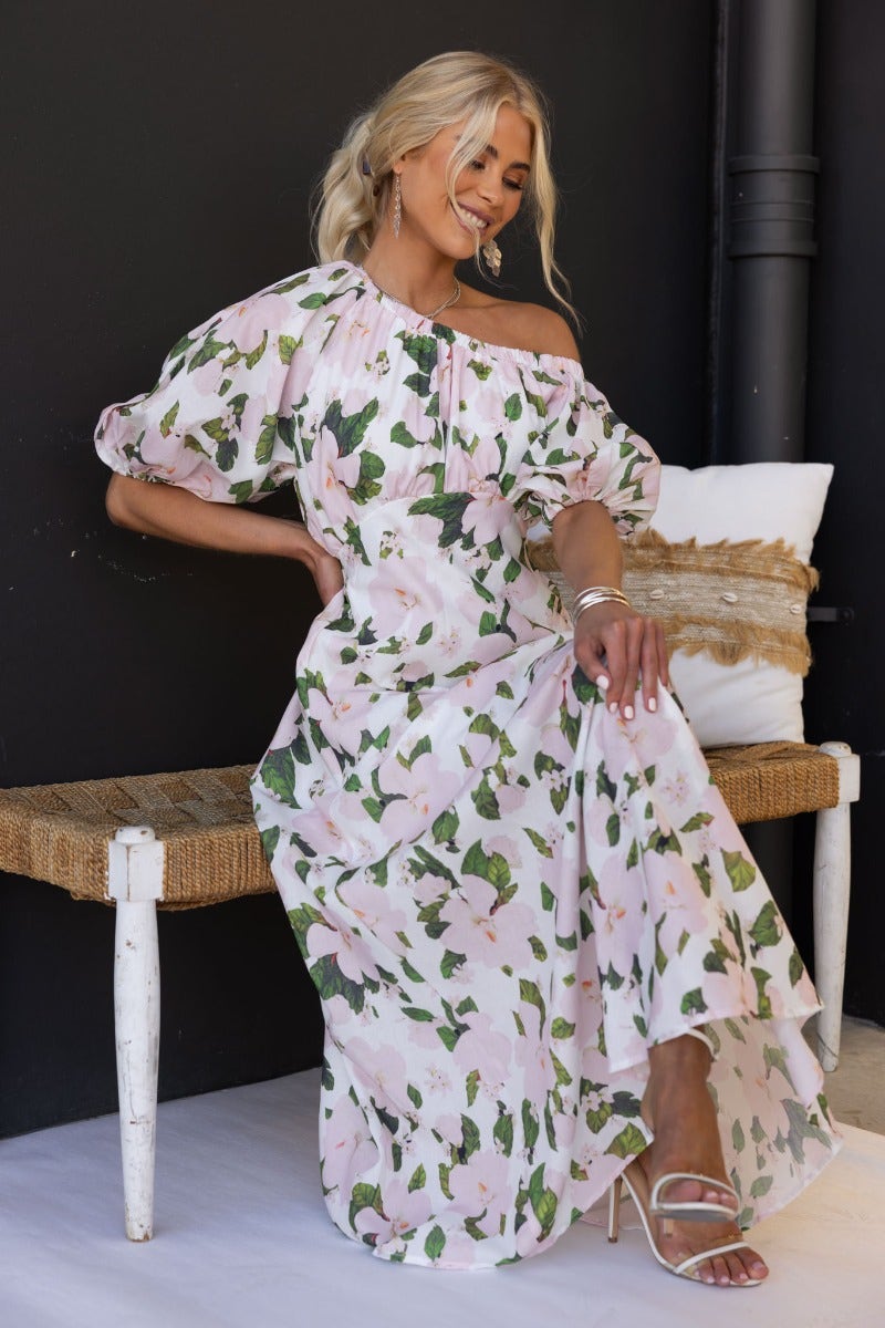 Floral print off-shoulder maxi dress with elastic neckline and cuff, model sitting on a bench.