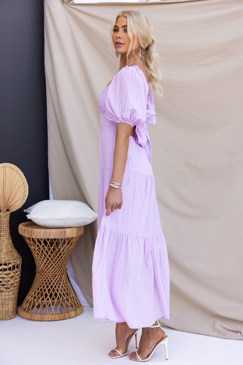 Nammos Maxi Dress in lavender with textured fabric, elastic sleeves, and a tied waist, displayed against a neutral backdrop.