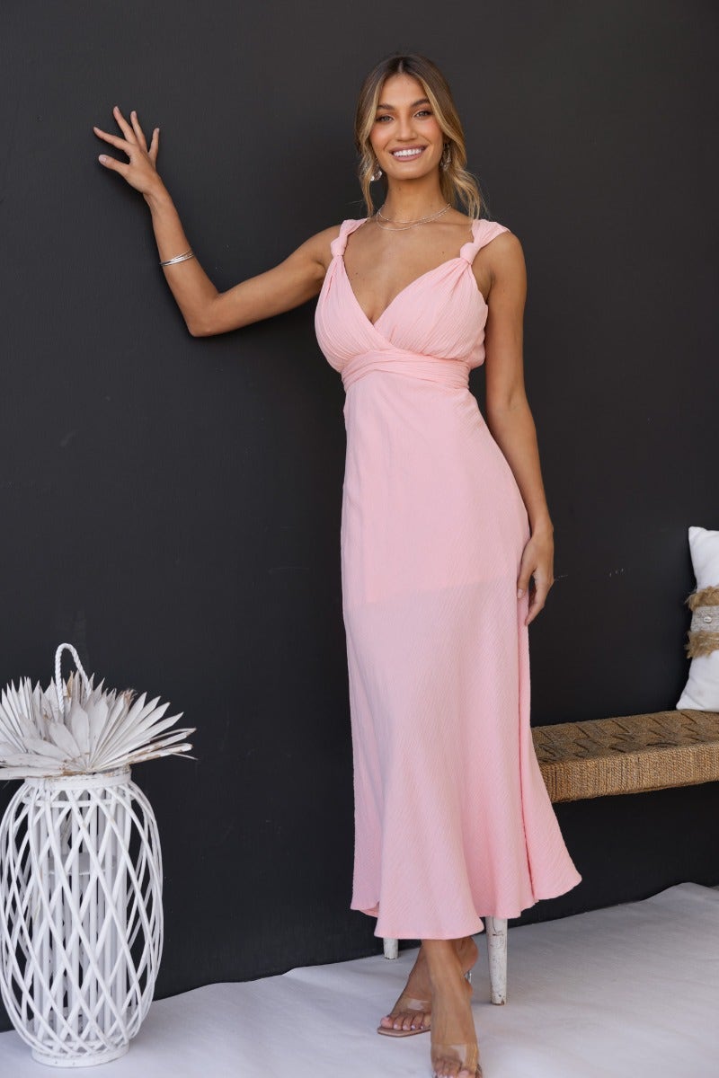 Model wearing a pink Gia Maxi Dress with textured material and tie detail, posing against a black background.