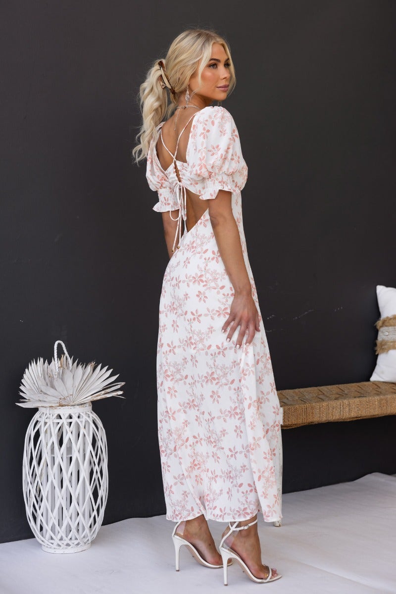 Back view of a woman in a floral print maxi dress with puff sleeves and an open tie back detail.