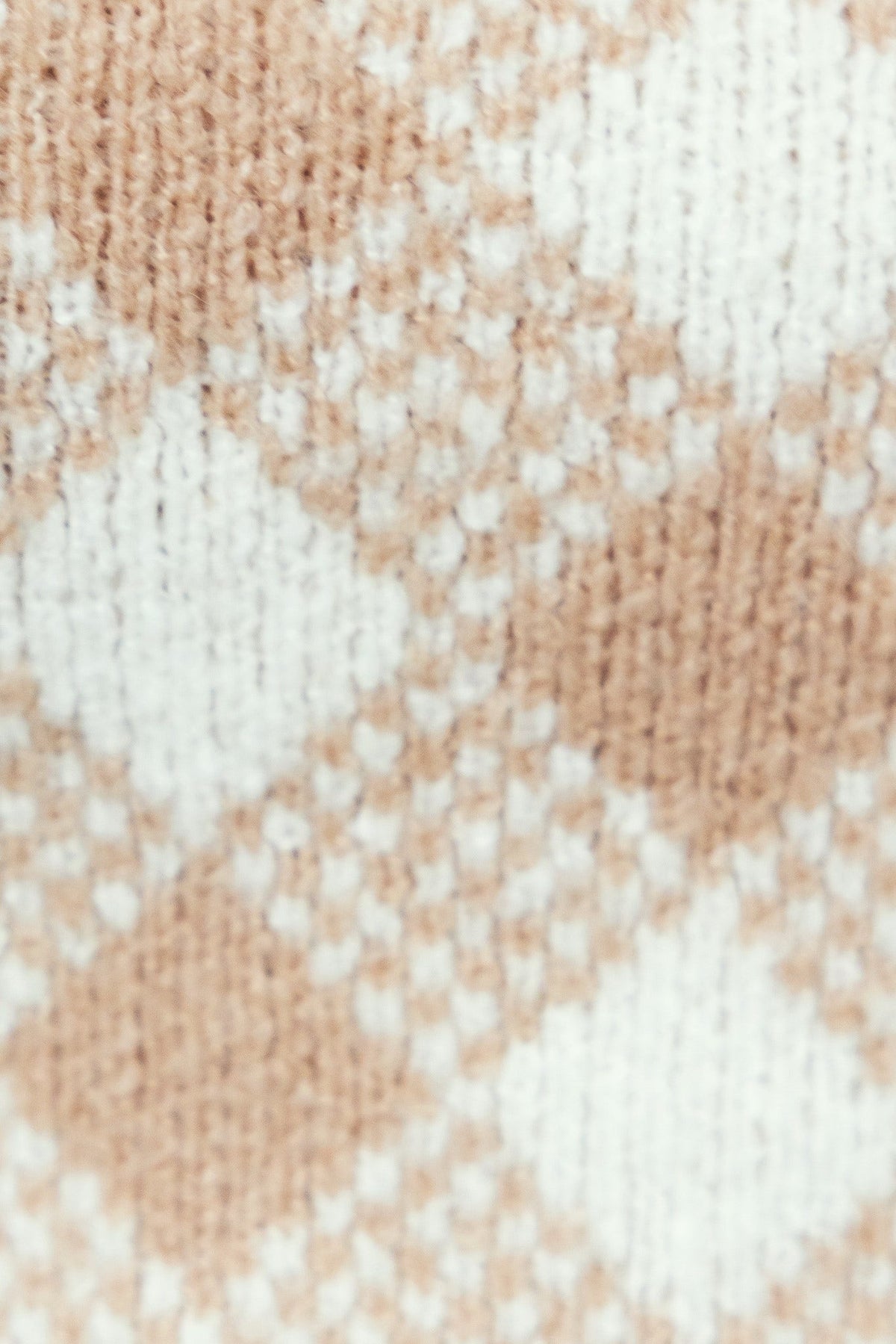 Close-up view of knitted fabric featuring a diamond pattern in beige and white colors, highlighting texture and detail.