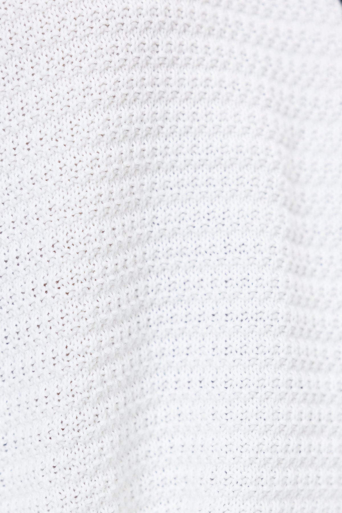 Close-up of textured white knit fabric featuring a breathable pattern, ideal for relaxed fit clothing.