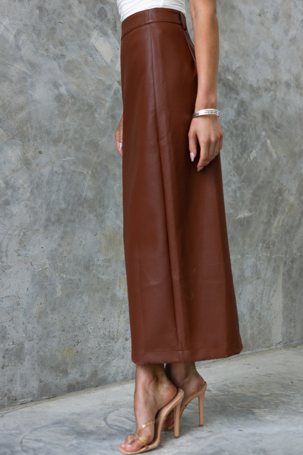 Model wearing a brown faux leather maxi skirt with a high waist, showcasing a stylish button-up front.
