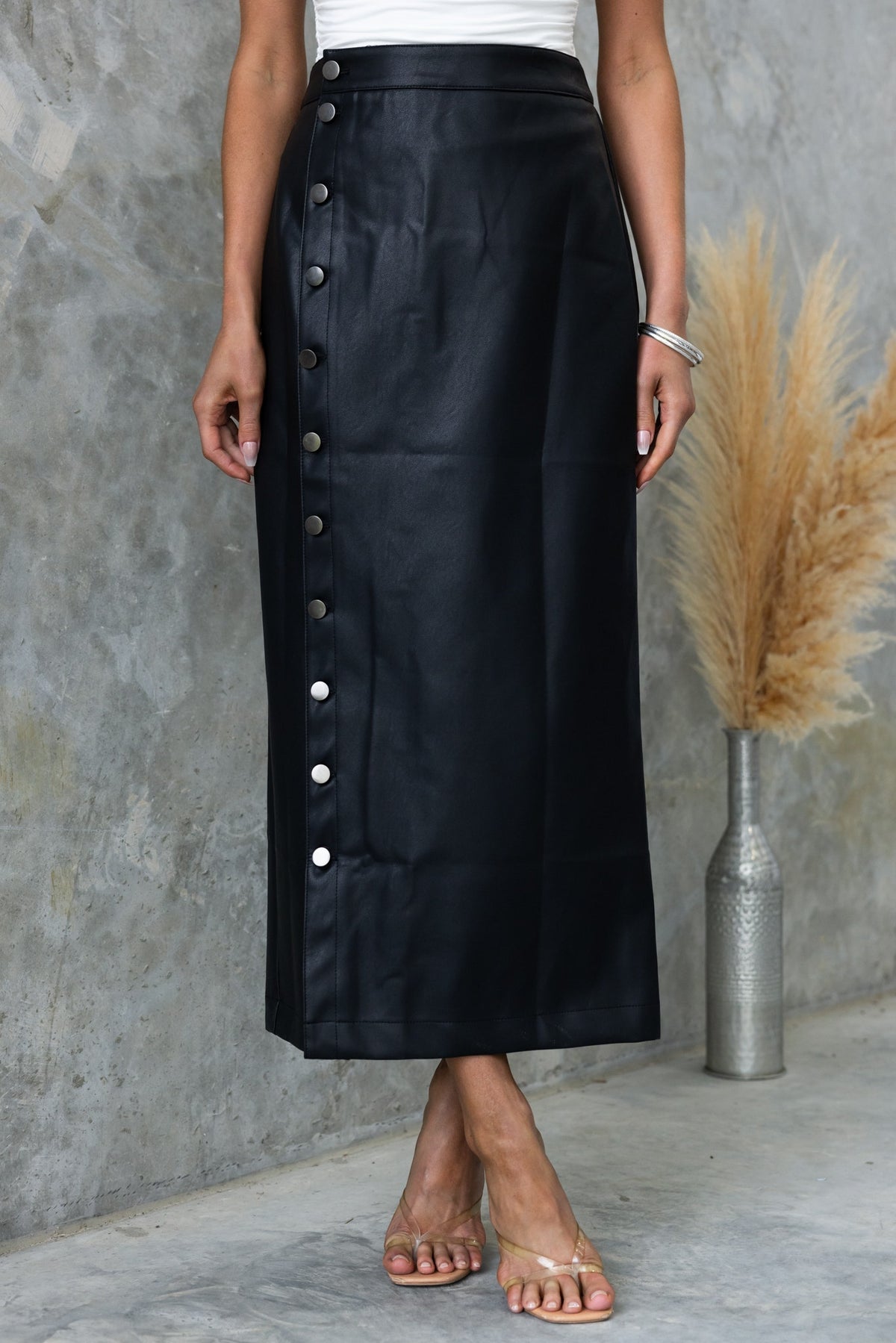 Black faux leather maxi skirt with button-up front and mid-high waist, styled with a fitted top and sandals.