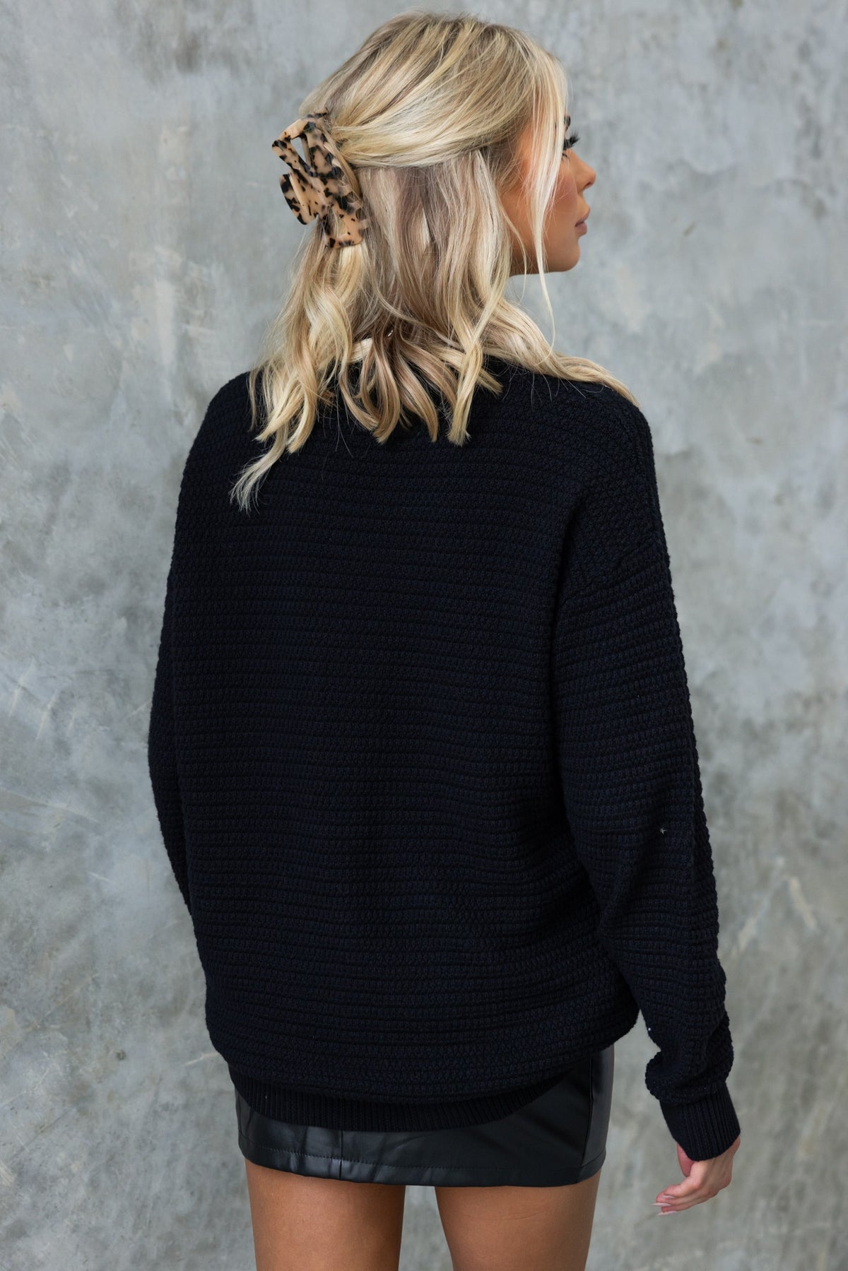 Back view of a woman in a black Rhode Jumper, featuring a relaxed fit and knit material, styled with a leather mini skirt.