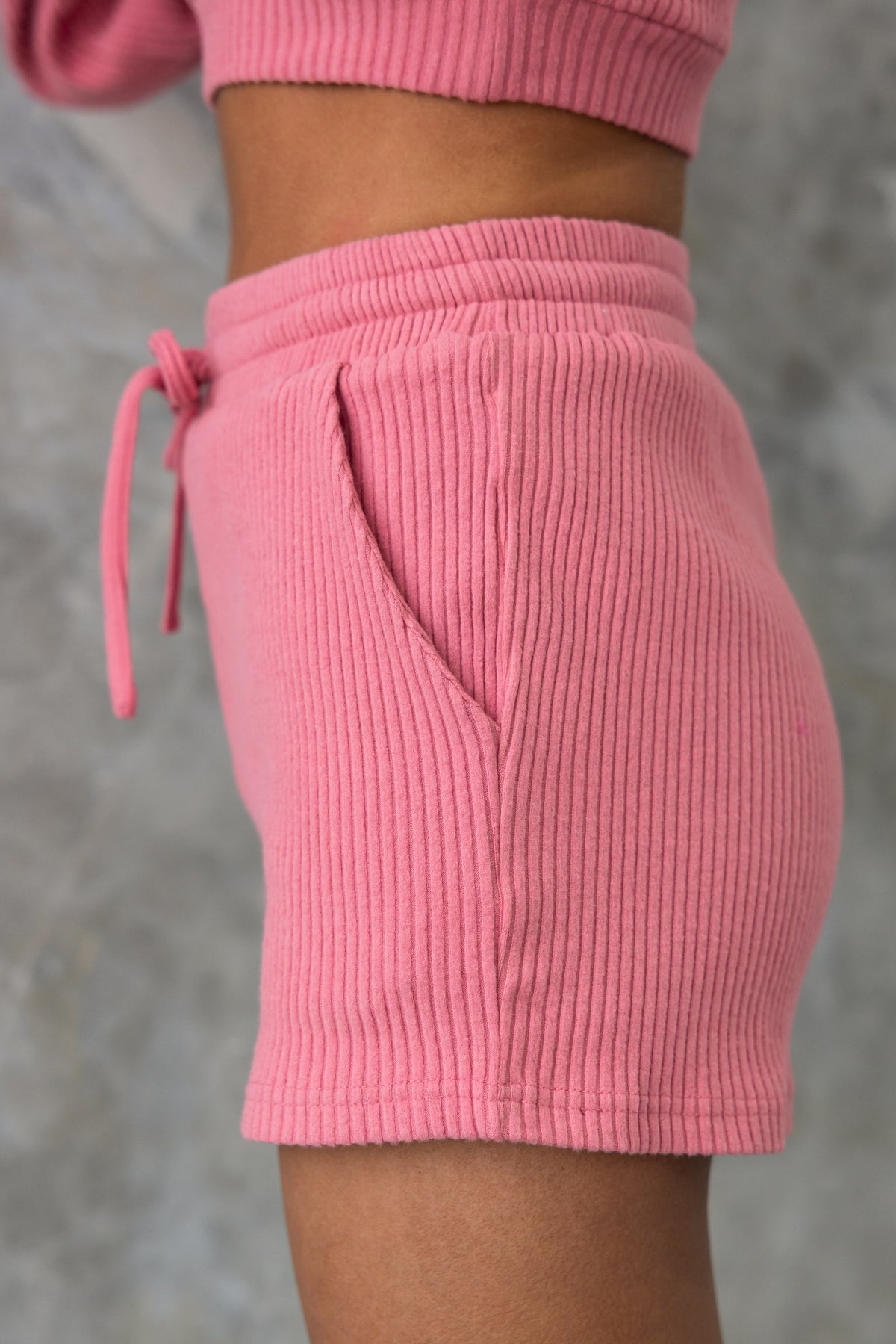 Side view of Mehki Shorts in ribbed pink fabric with elastic waistband and pockets.