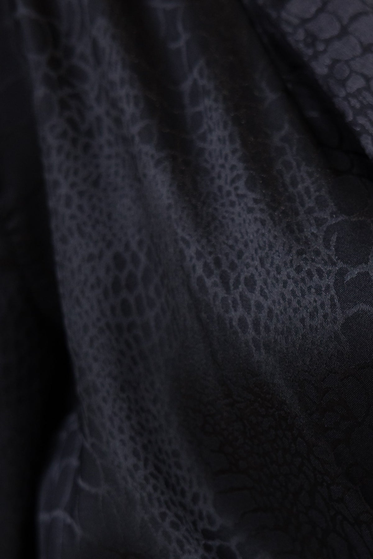 Close-up of embossed black satin fabric featuring a reptile pattern, highlighting the elegant texture.