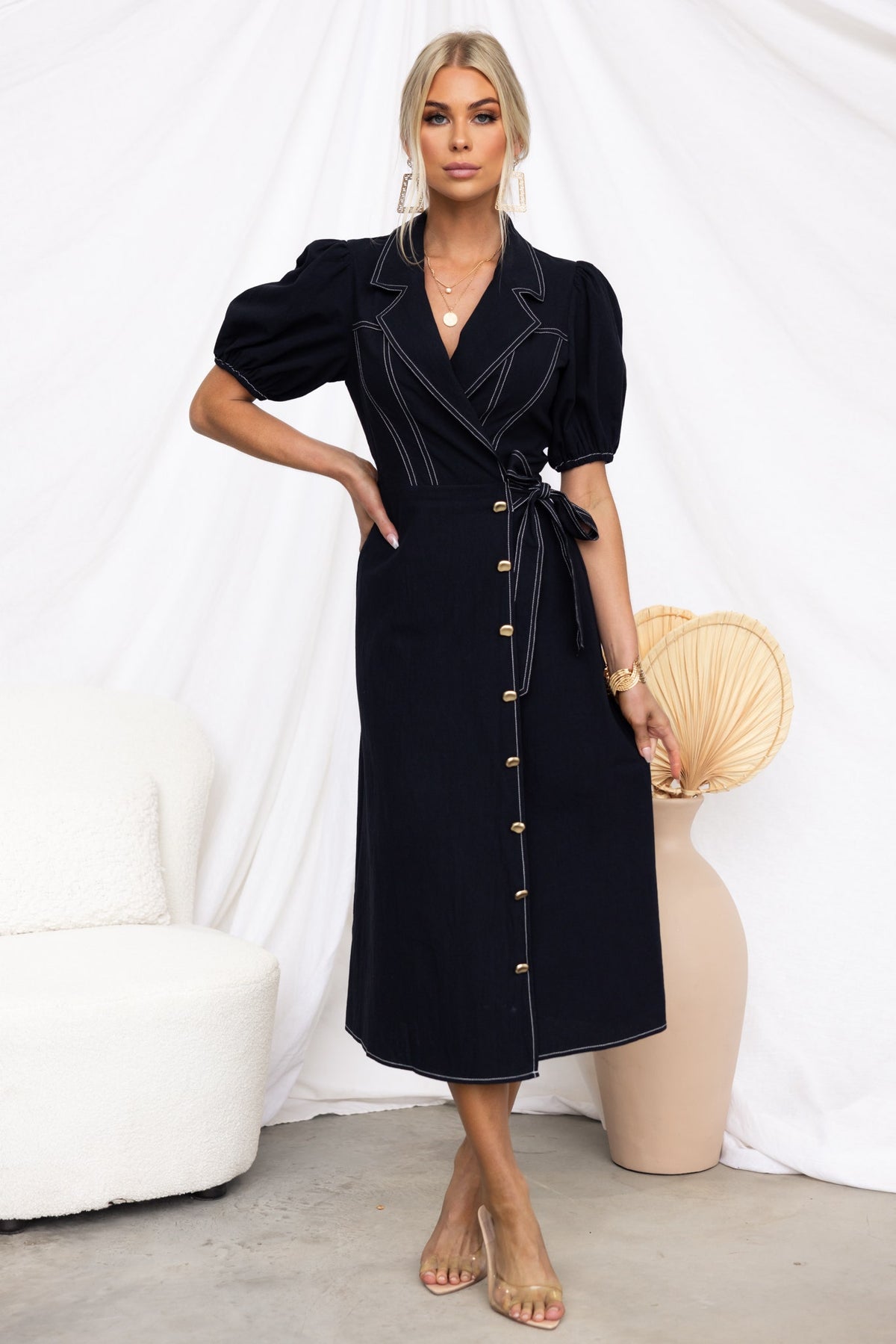 Model wearing a black Sharnee Wrap Midi Dress with collar, elastic sleeves, faux buttons, and asymmetric hem.