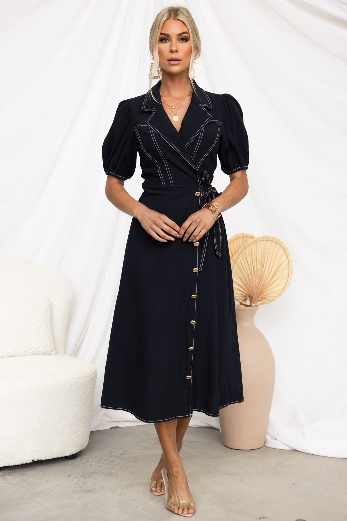 Sharnee Wrap Midi Dress in black with puff sleeves, tie details, faux buttons, and asymmetric hem, styled on model.