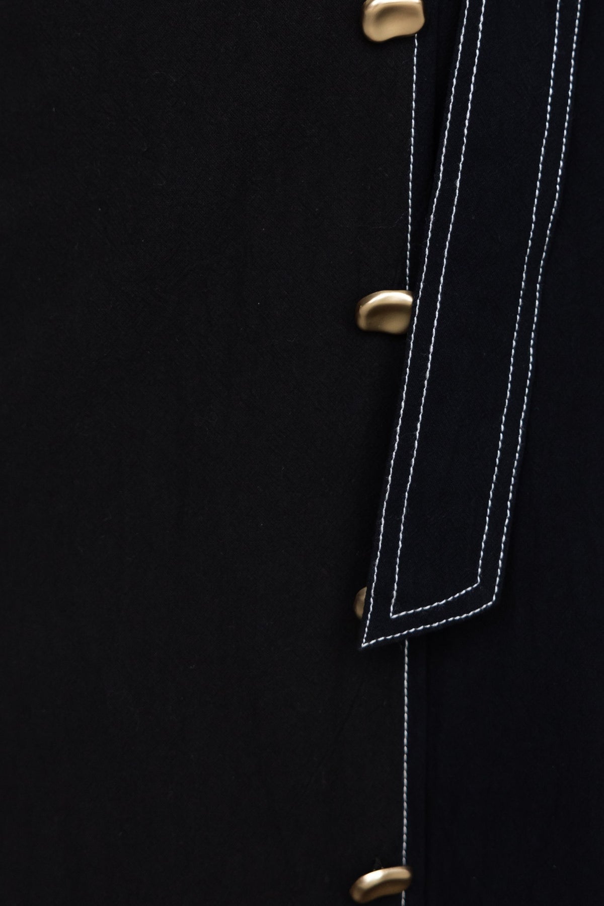 Close-up of black midi dress with faux buttons, tie detail, and contrasting stitching.