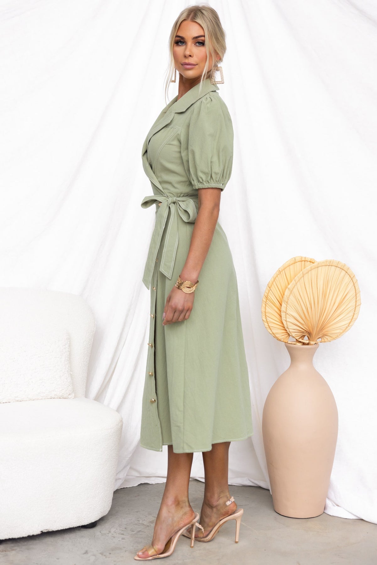 Model in a green Sharnee Wrap Midi Dress with tied waist, faux buttons, and asymmetric hem, styled with minimal accessories.
