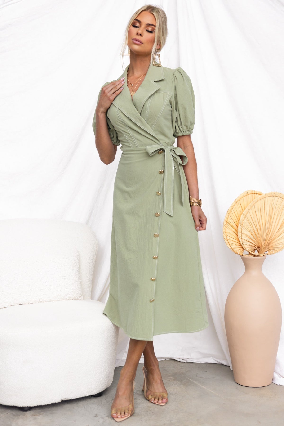 Model wearing a light green Sharnee Wrap Midi Dress with puff sleeves and faux buttons, styled with a minimalist backdrop.