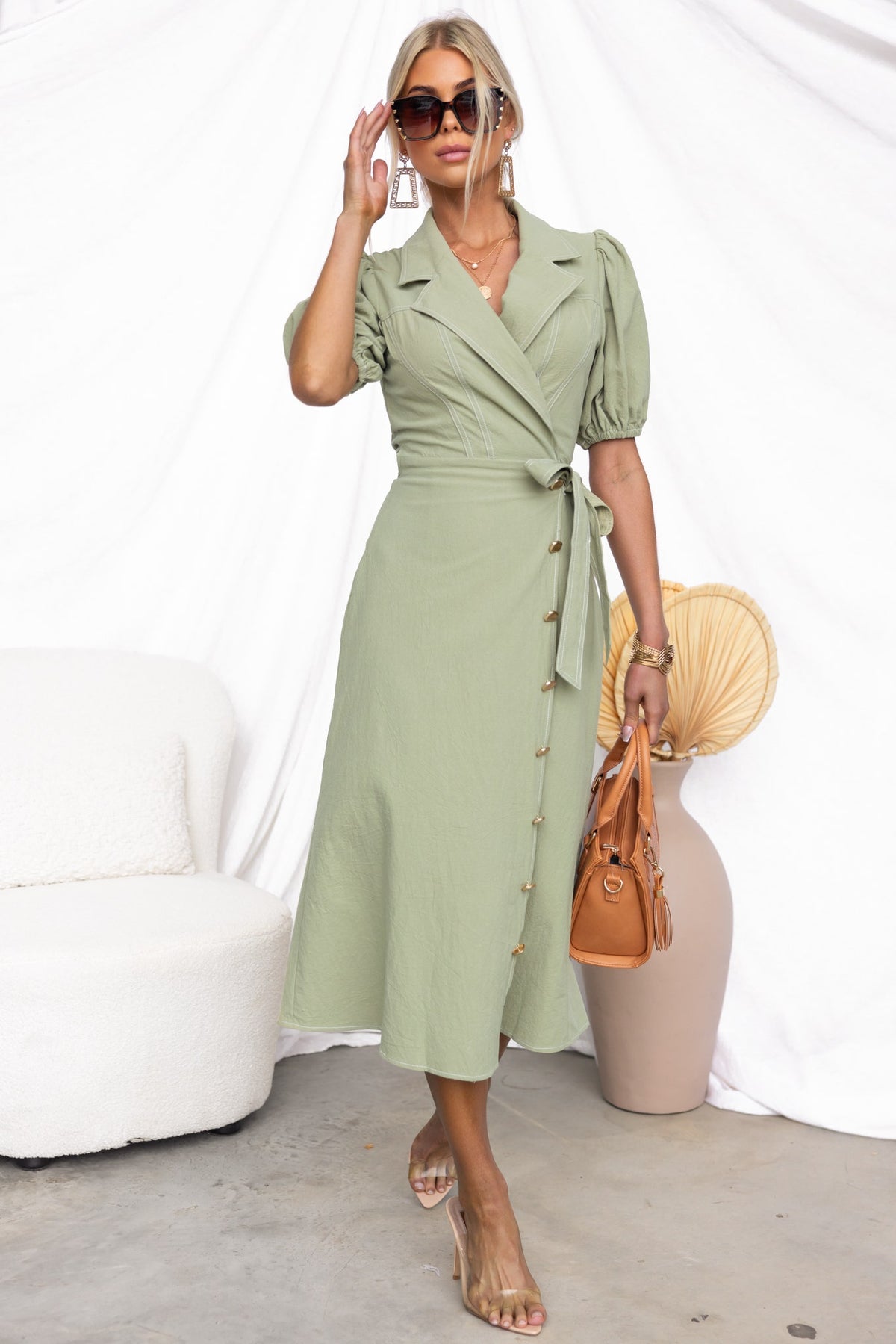 Model wearing a stylish green Sharnee Wrap Midi Dress with puff sleeves, faux buttons, and an asymmetric hem.