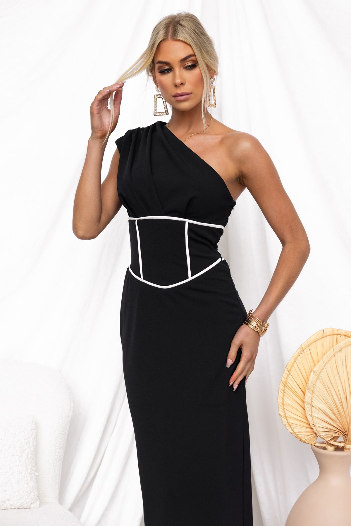 Elegant black Vega Maxi Dress with one-shoulder neckline and fitted bodice, model poses against a minimalist background.