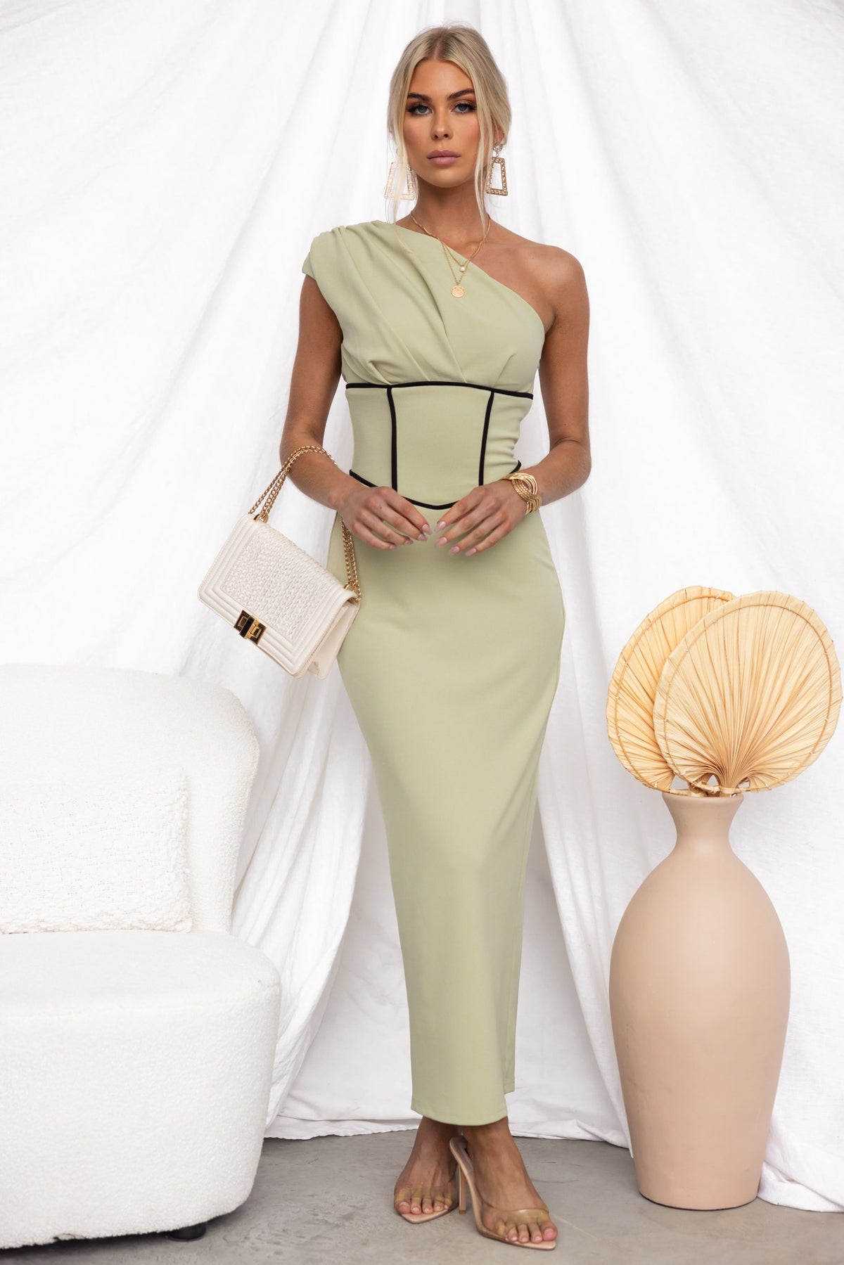 Model wearing a green Vega Maxi Dress with one-shoulder neckline and elegant back split, styled with a handbag.