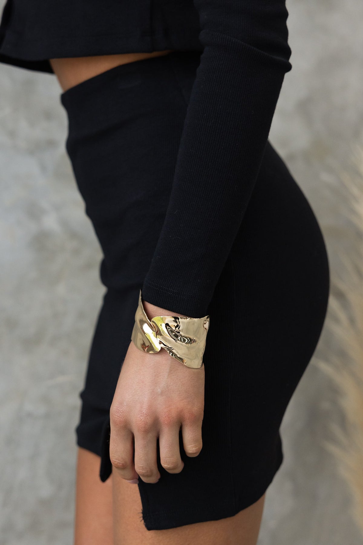 Model wearing a black mid-high waist skirt with an elastic waistband and gold cuff bracelet.
