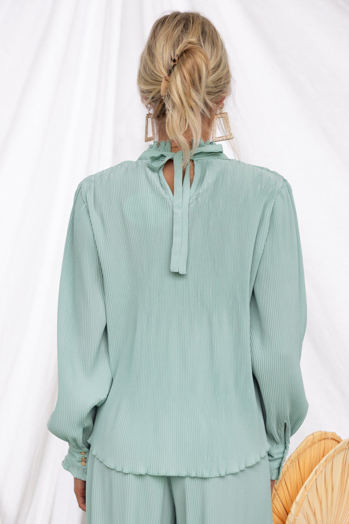 Back view of the Barbara Top in mint green, showcasing pleated material and a tie at the neck.