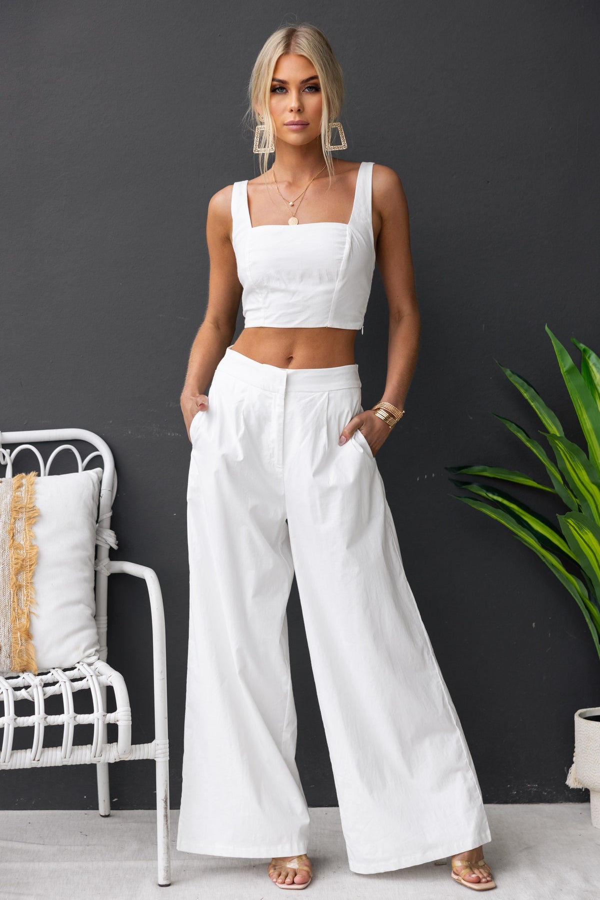 Janae Top with square neckline and adjustable straps, paired with wide-leg white pants, model standing against a dark wall.