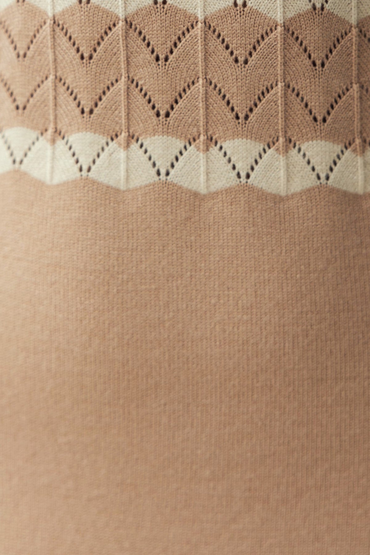 Close-up of textured knit fabric with a patterned design in soft beige and cream colors.
