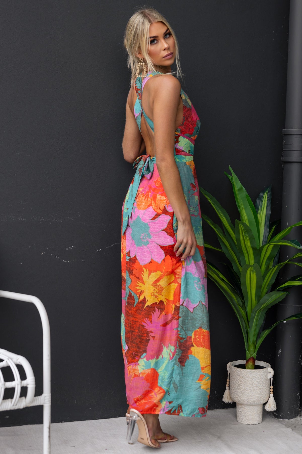 Kyrie Maxi Dress featuring adjustable tie neckline and vibrant floral print, model shown from the back with plants in the background.
