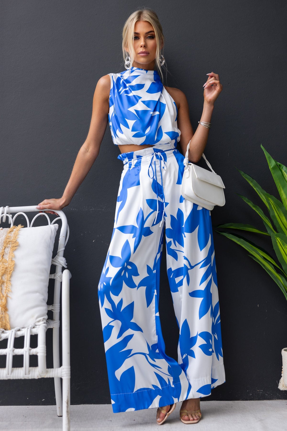 Model wearing the Dreamie Set, featuring blue floral print satin top and wide-leg pants, styled with a chic handbag.
