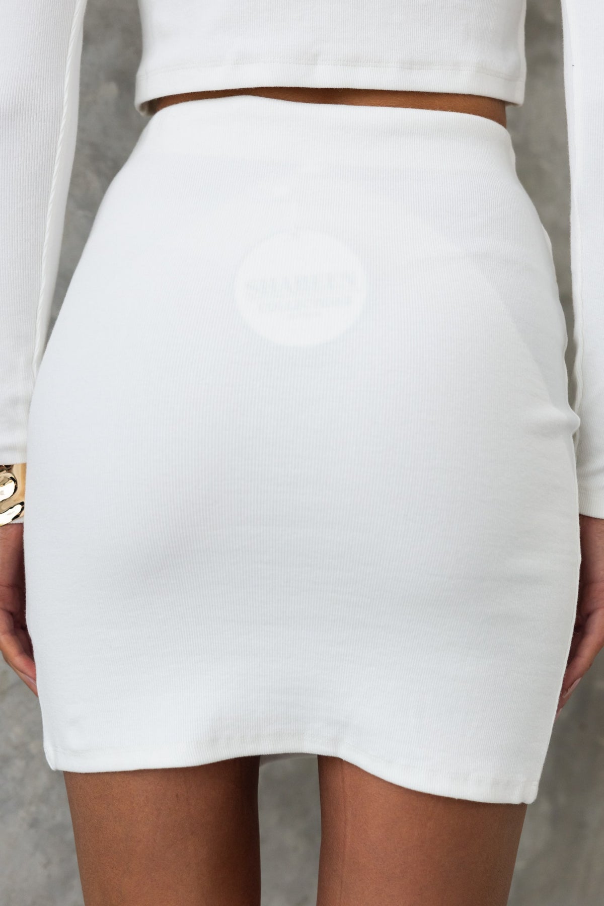 Back view of a white mid-high waist skirt with elastic waistband and front split, showcasing its ribbed stretch material.