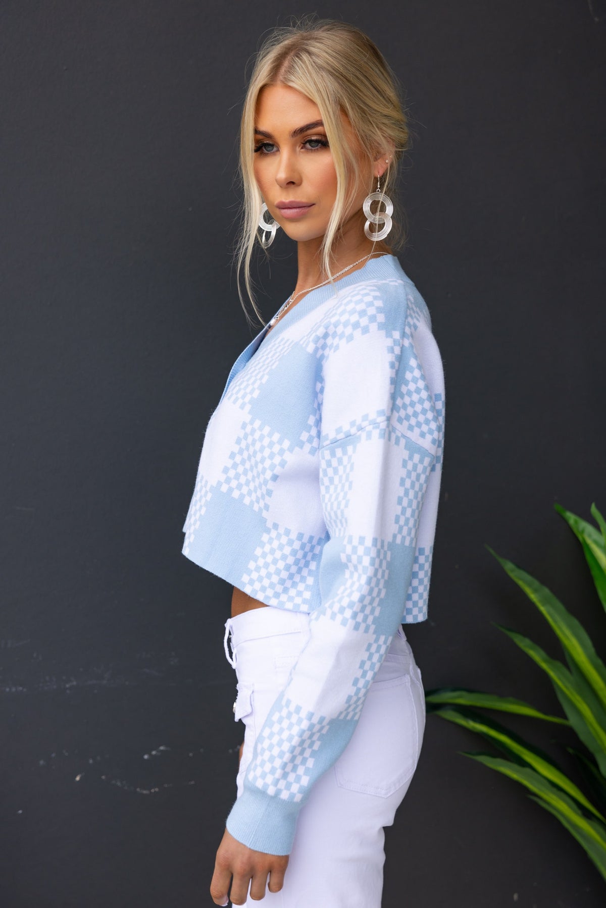 Side view of a stylish Roni Cardigan with a blue checkered pattern, paired with white pants, model wearing statement earrings.