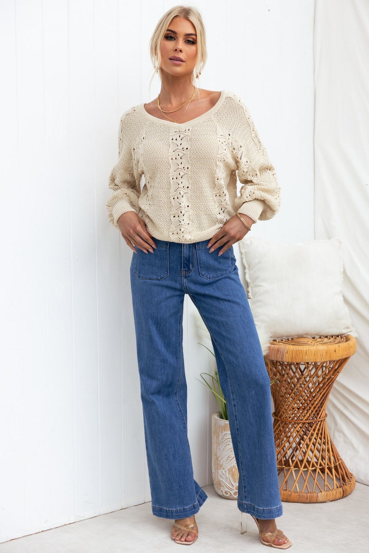 Model wearing a relaxed-fit cream knit top with V-neckline and blue wide-leg jeans, styled in a chic indoor setting.
