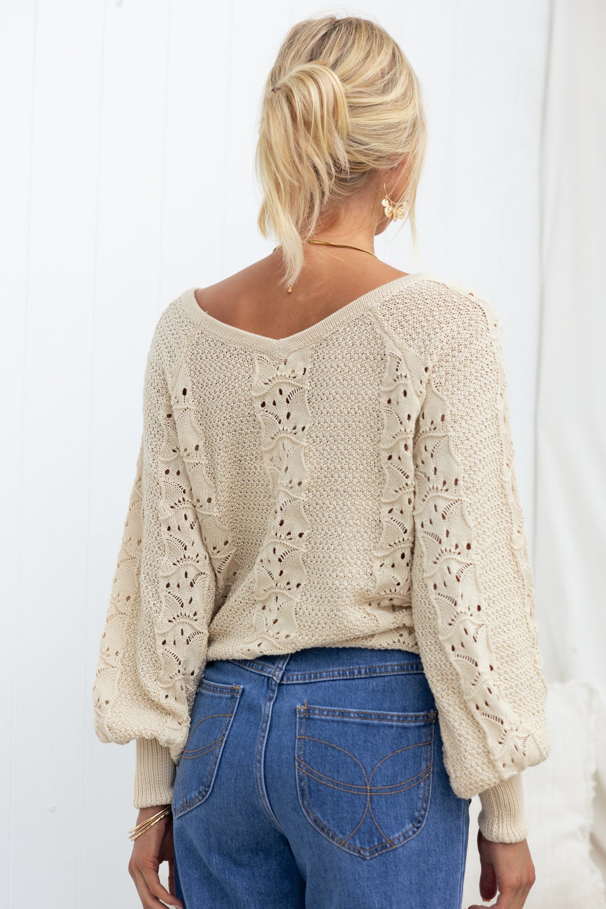 Back view of a model wearing the Cadie Knit top with a V-neckline and semi-open weave, paired with jeans.