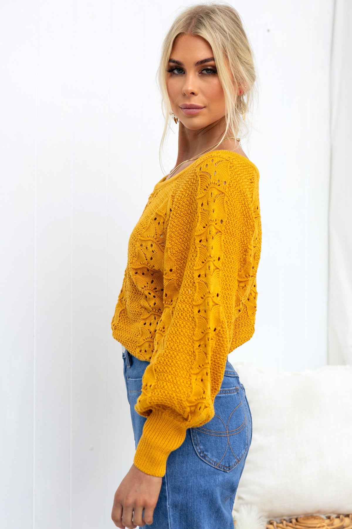 Side view of model wearing a yellow Cadie Knit top with open weave design and relaxed fit, paired with blue jeans.