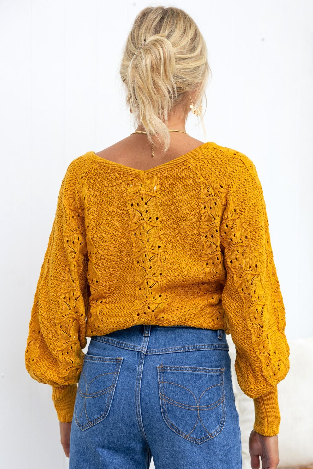 Back view of a woman wearing a mustard yellow Cadie Knit top with a V-neckline and balloon sleeves.