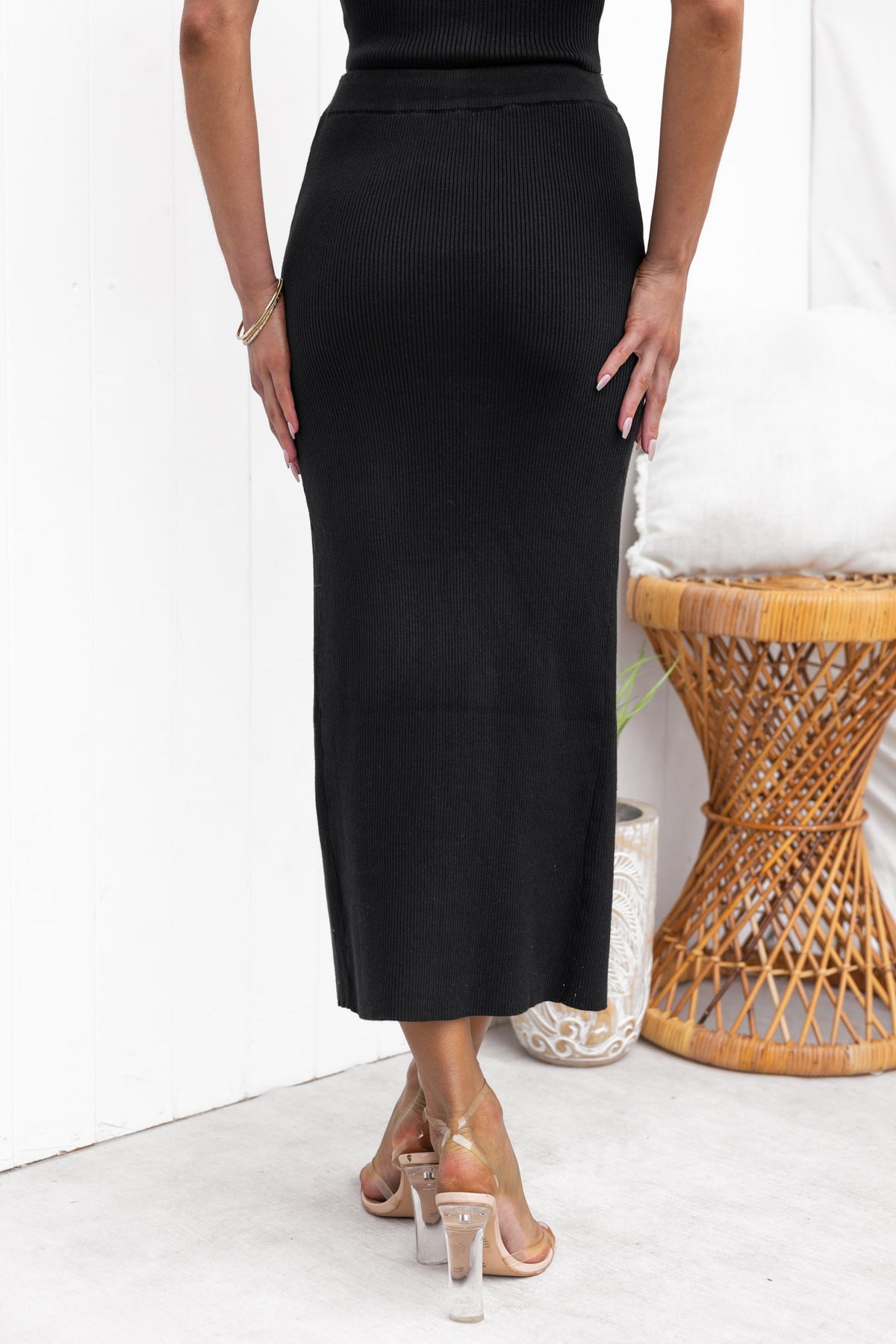Back view of Estha Maxi Skirt in black with an elastic waistband and front split, styled with strappy heels.